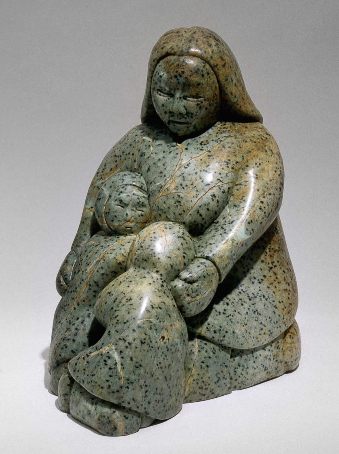 A soapstone sculpture of a mother holding two of her children.