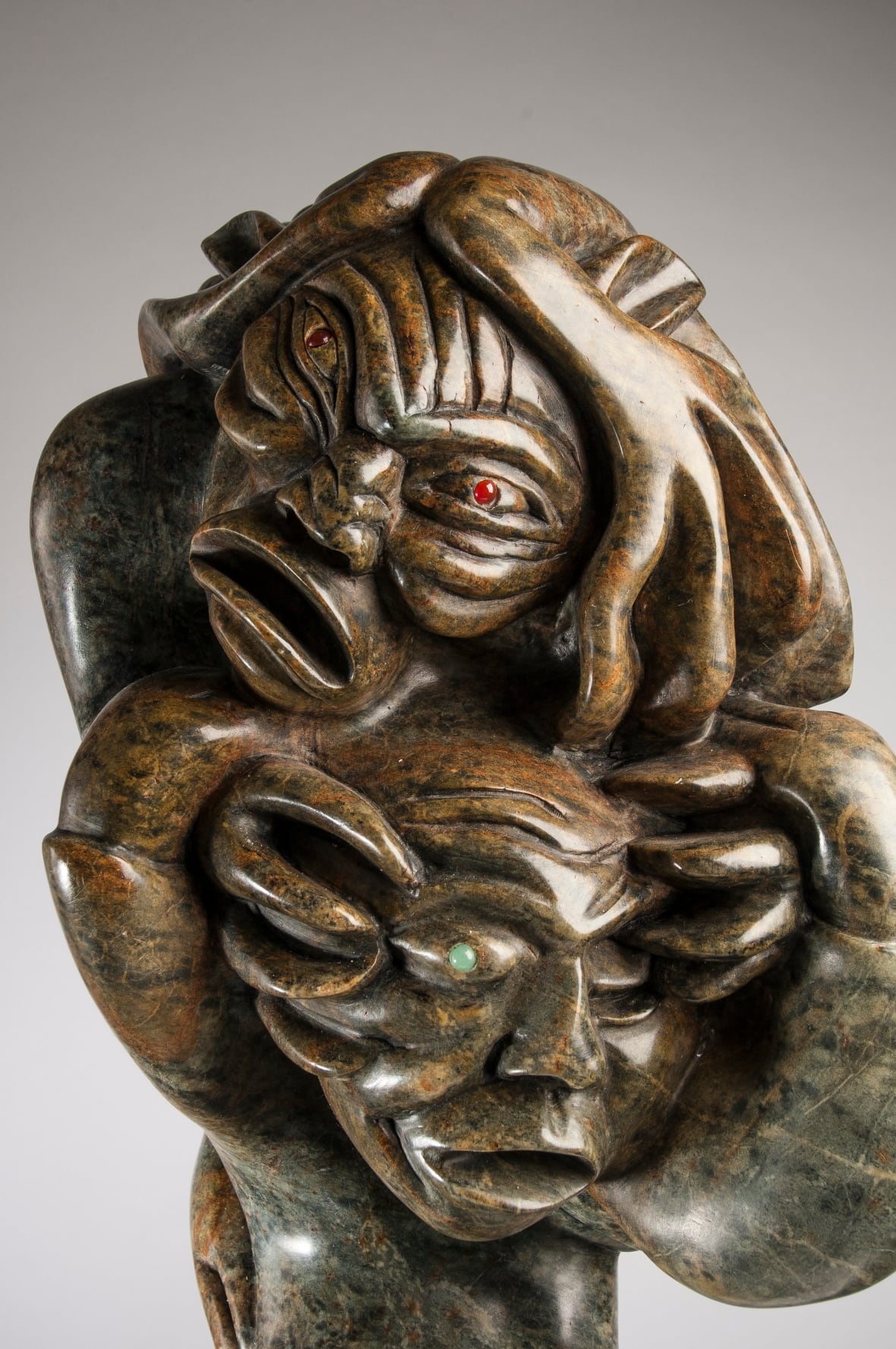 A demon with red eyes clutches at the face of another demon with green eyes.