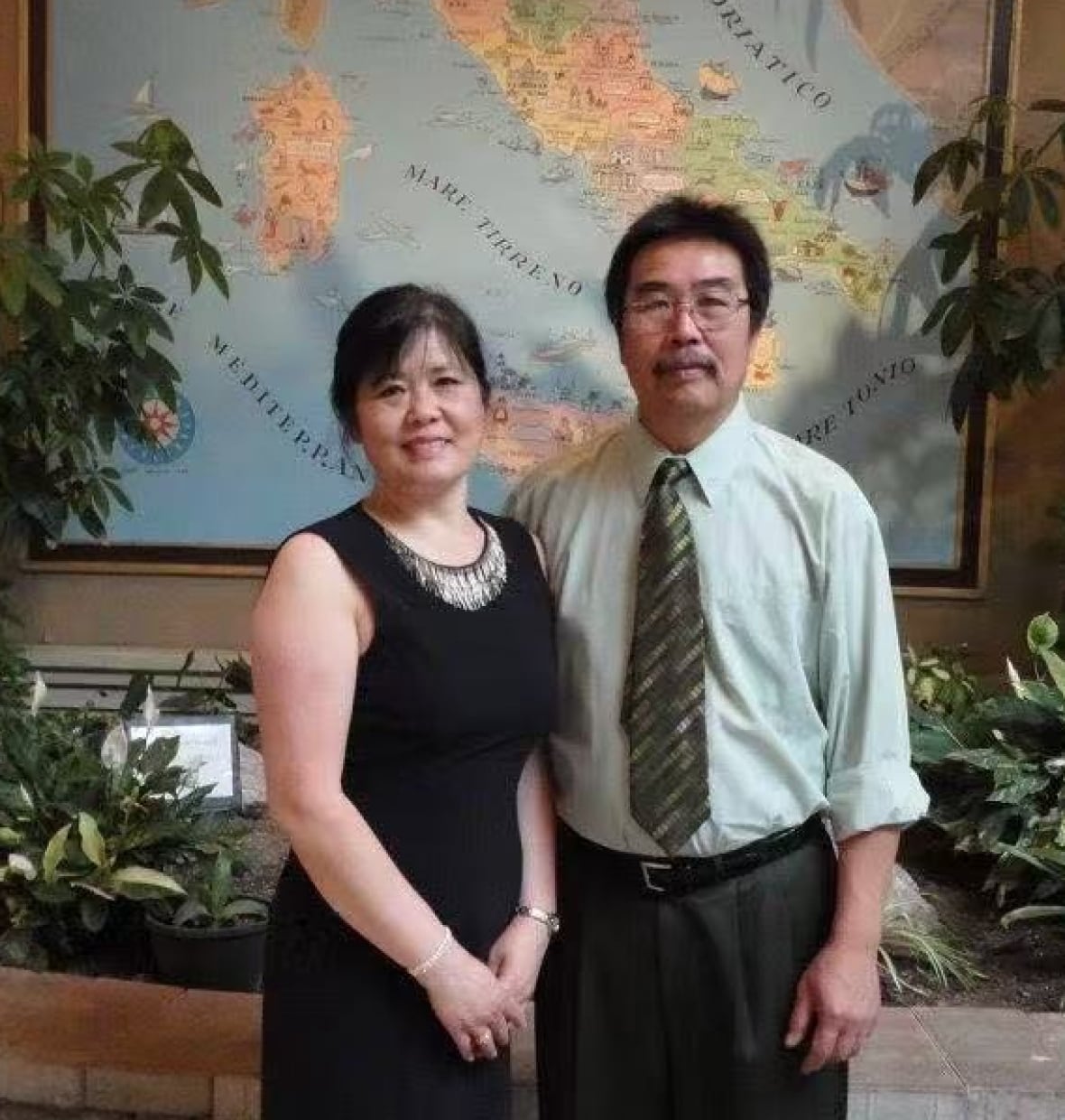 A man and a woman pose in front of a world map.