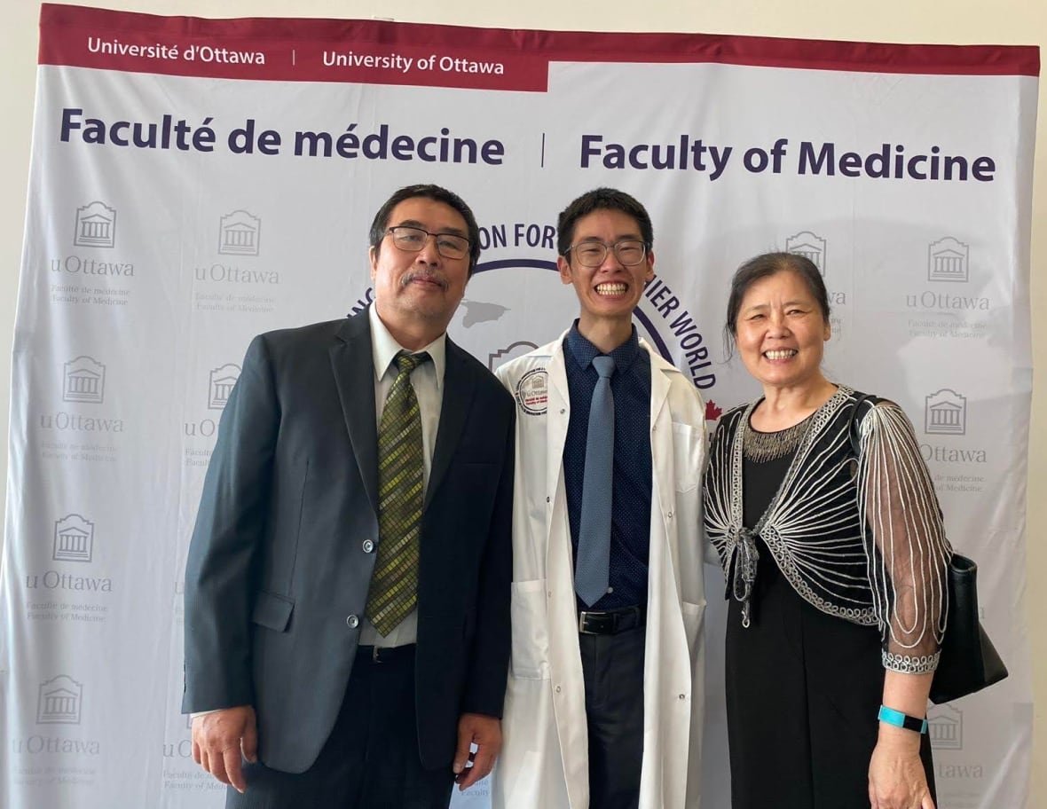 A couple stands proudly next to a young man in a white coat.