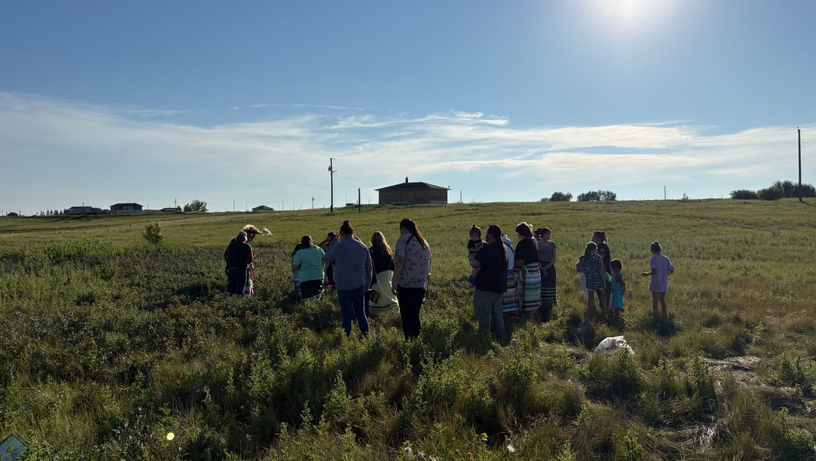 Roughly a dozen people stand in a field.