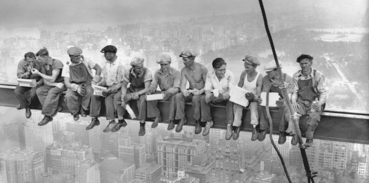 Men sit on a beam high up in the air in a black and white photo.