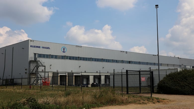 A big gray warehouse behind a chainlink fence