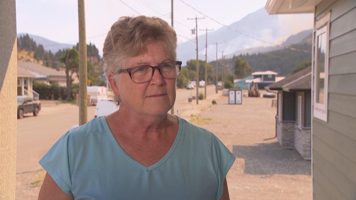A woman with short blond hair and glasses is outside, dressed in a blue shirt.