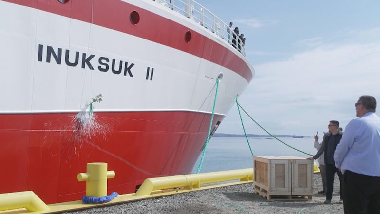 people watch as a bottle breaks on the side of the ship