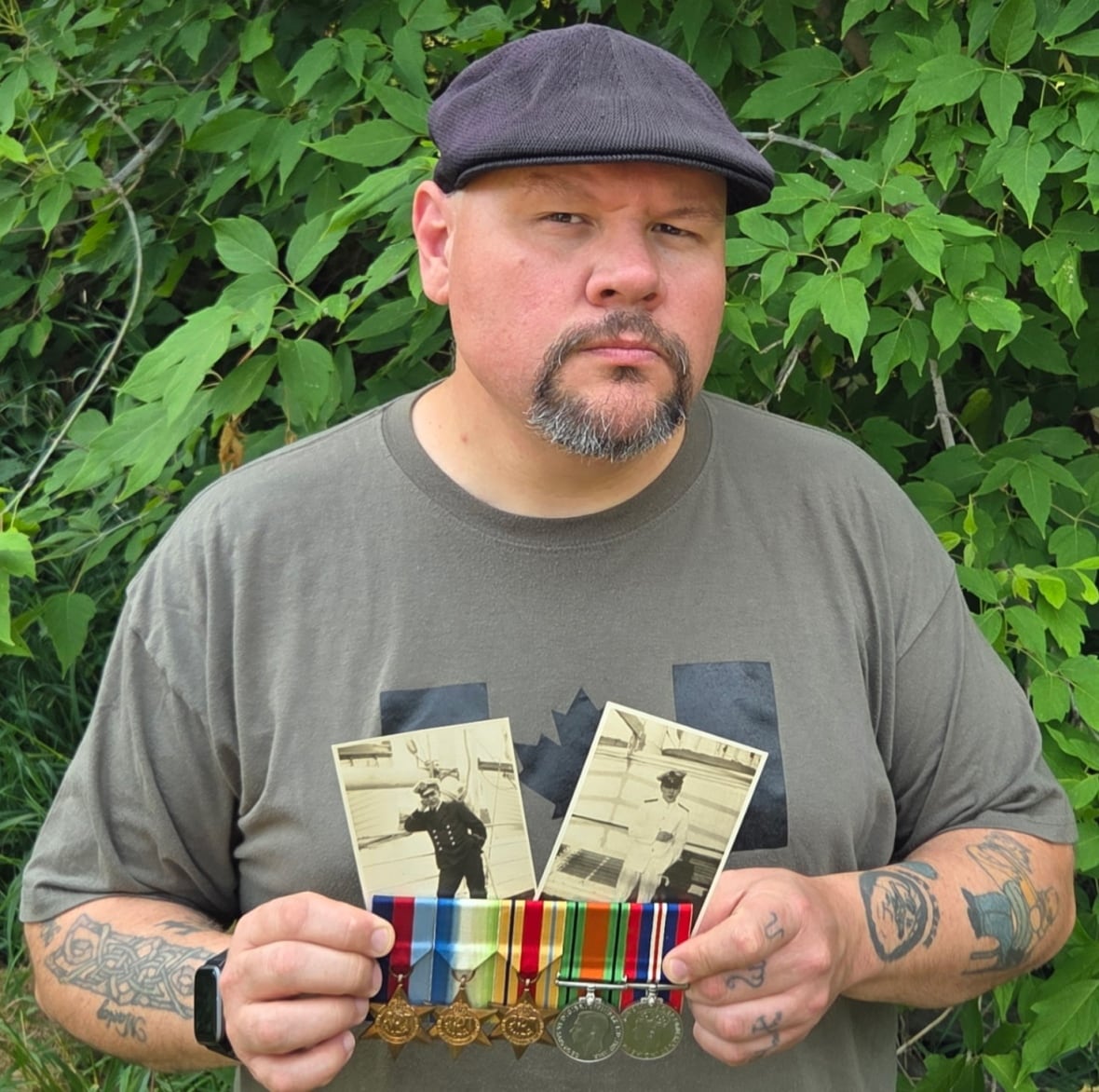 A man standing holding two black and white photos and military medals.