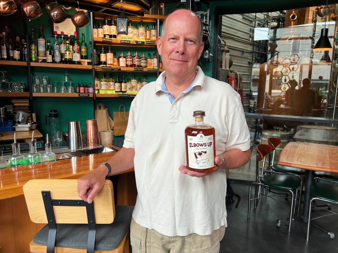 Un hombre blanco que lleva una camisa de golf calvo tiene una botella de licor hecha en la instalación que trabaja como presidente.