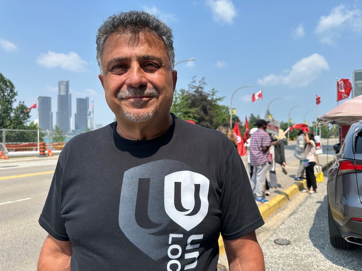 A man wearing a Unifor shirt with stiking workers in the background.