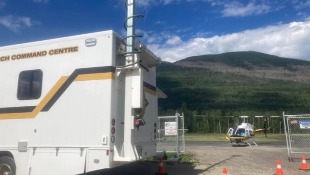 A photo of a search and rescue vehicle and a helicopter with a mountain in the distance.