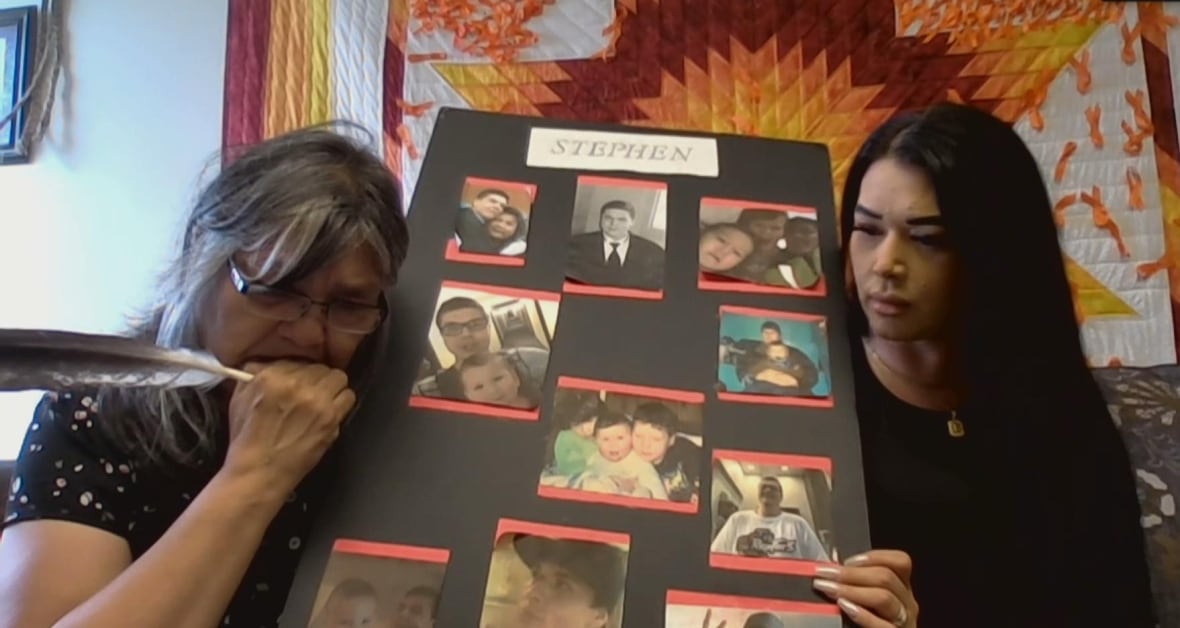 Two women hold a black poster featuring photos of a man who died of cancer.