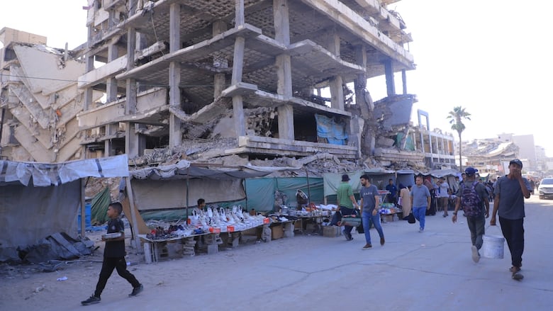 People walk past a large damaged building. 