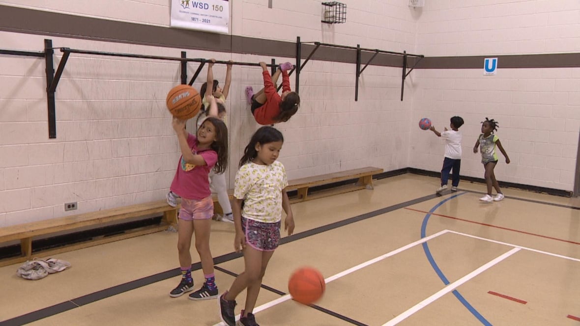 A group of children play in an indoor basketball court.