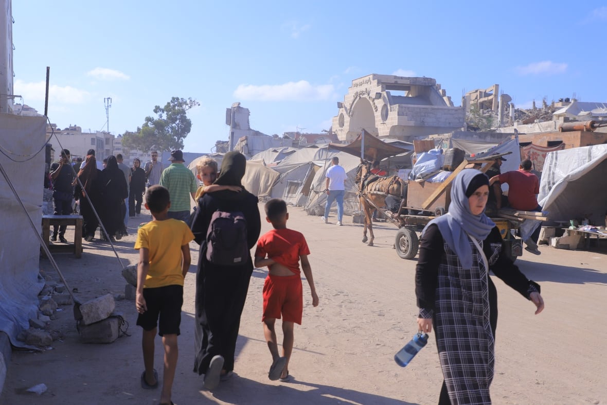 Peoplk walk on a street, as a hors-drawn cart is seen in the background.
