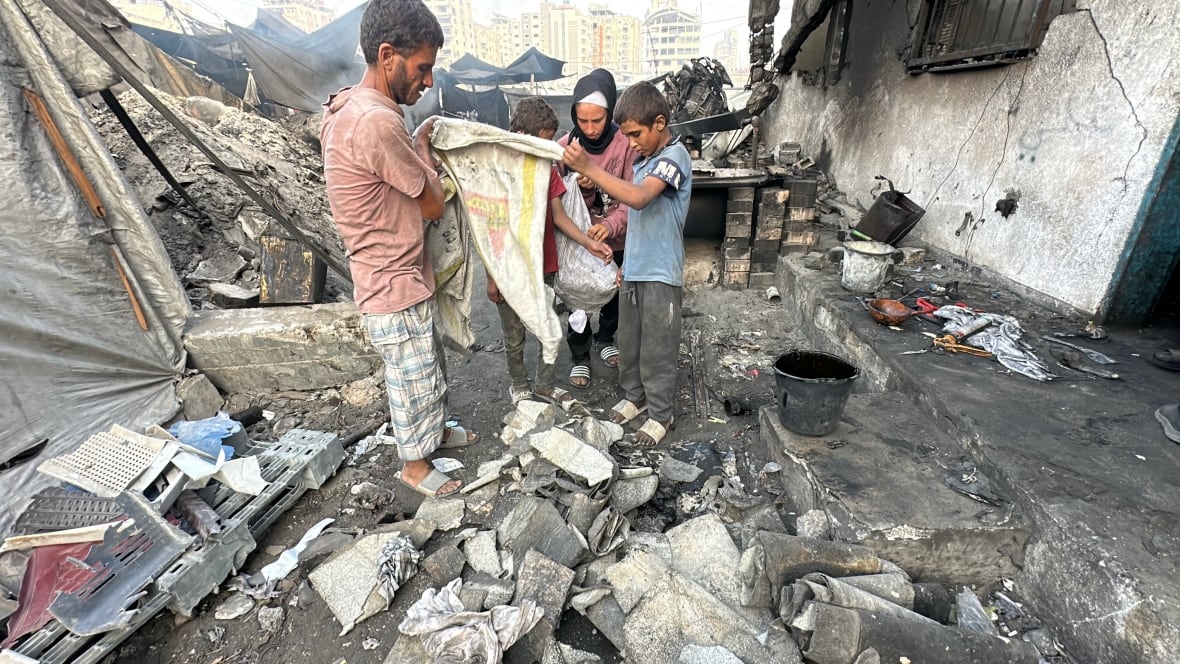A man and three children stand among rubble as they empty bags of scrap piece of cloth. 