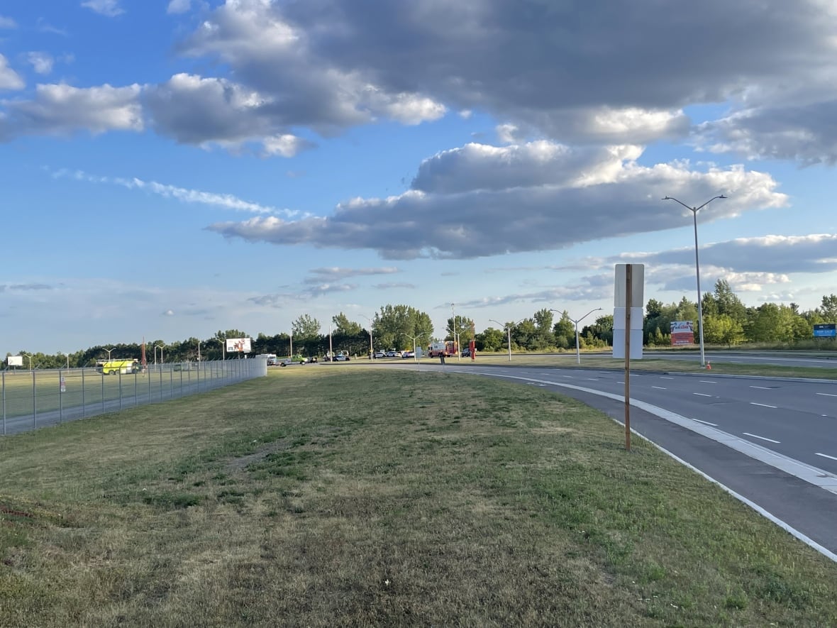A grassy patch with a road off to the side and several emergency vehicles in the distance.
