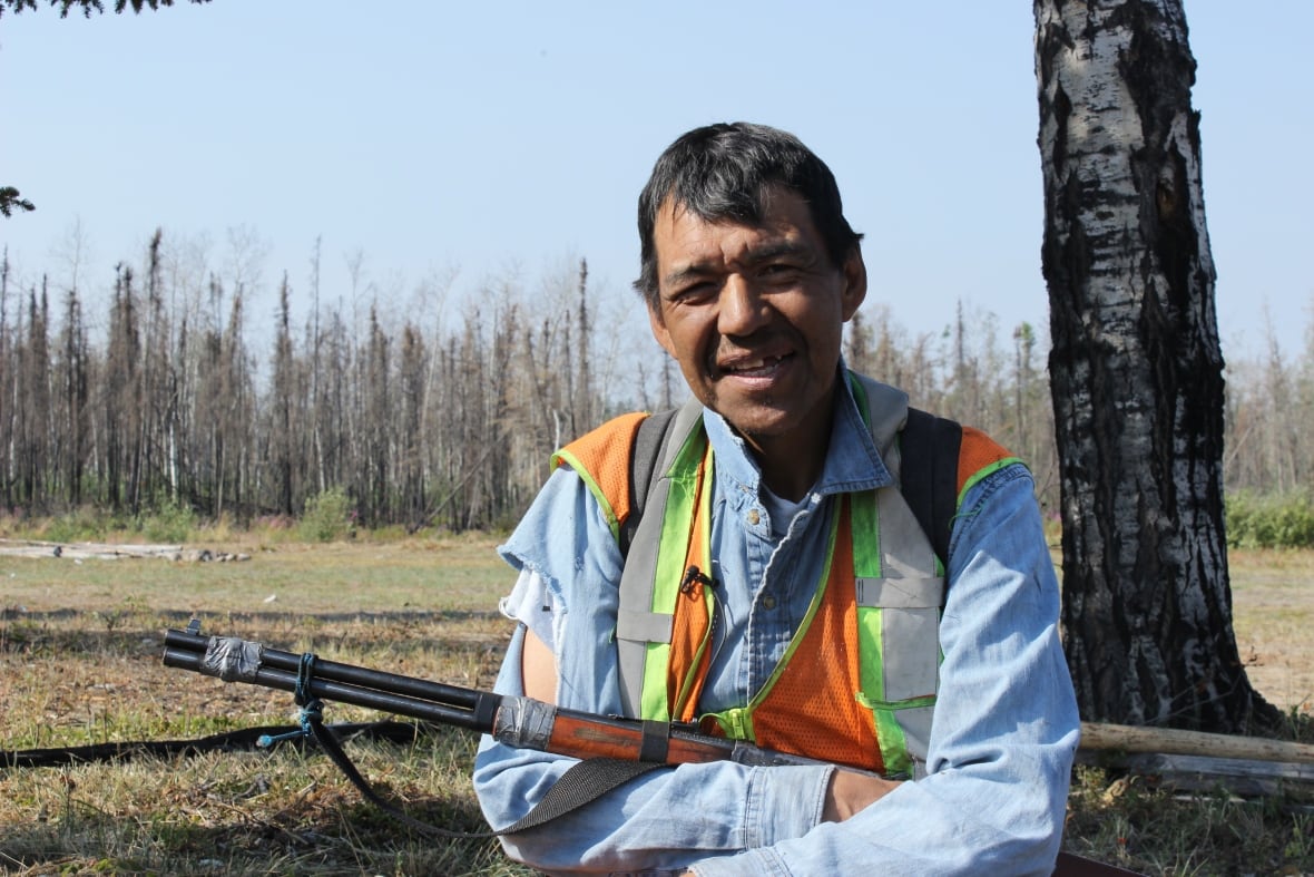 A man holding a rifle to his chest, squinting into the sun.