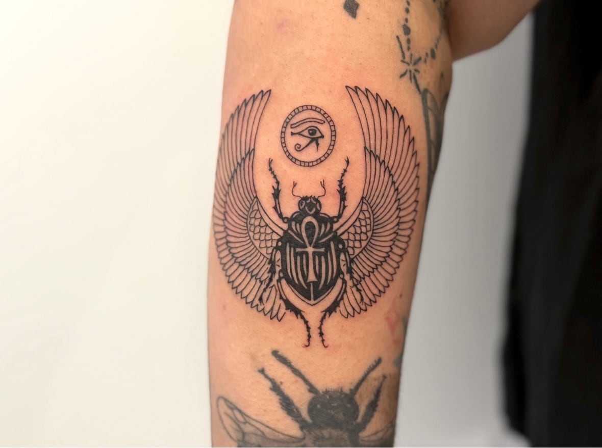 A beetle in Lenton's right forearm. Everything is black and surveyed among several other tattoos. 