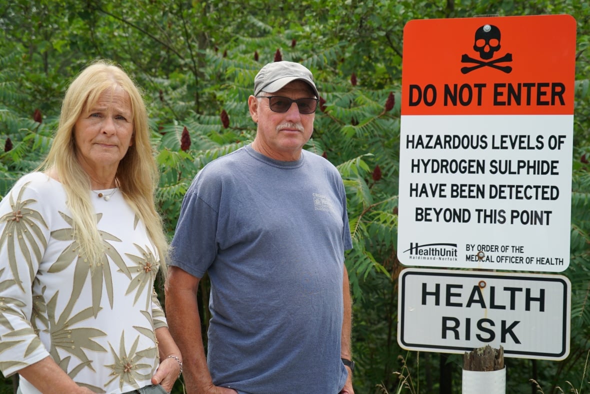 Paula Jongerden, left, and John Spanjers stand beside one of several signs along Forestry Farm Road that warn of the serious threat that looms just past the fenced off area.