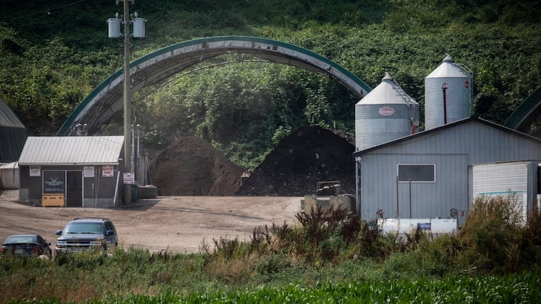 A peaked-roof metal building with two silos and a separate building with a car parked in front of it on a rural property