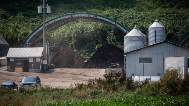 A peaked-roof metal building with two silos and a separate building with a car parked in front of it on a rural property