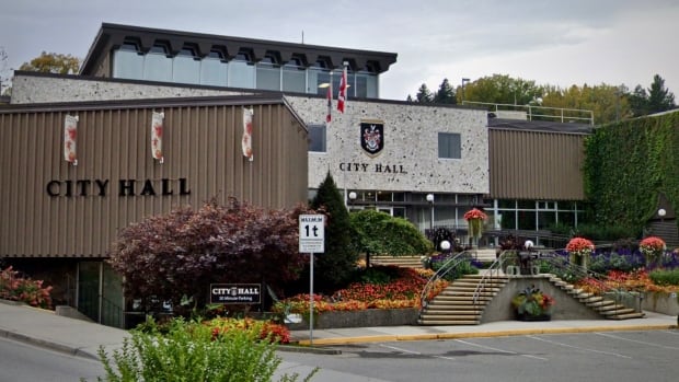 a municipal building with many flowers and flags. It says city hall on two walls and a sign.