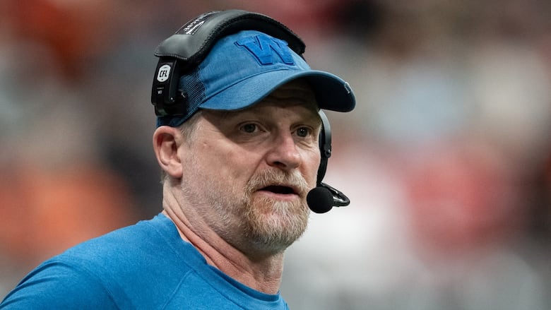A man in a blue shirt and blue cap speaks into a headset.
