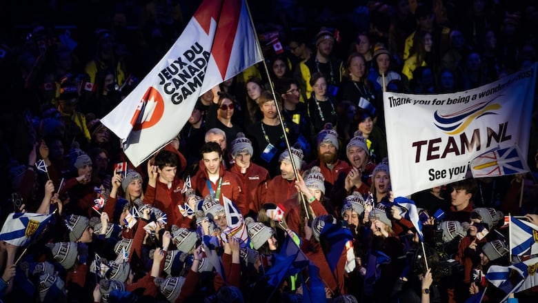 A large group of athletes are shown holding Newfoundland and Labrador flags, plus a large Canada Games flag, and a banner that reads 'Thank you for being a wonderful host; TEAM NL; See you in 2025.'
