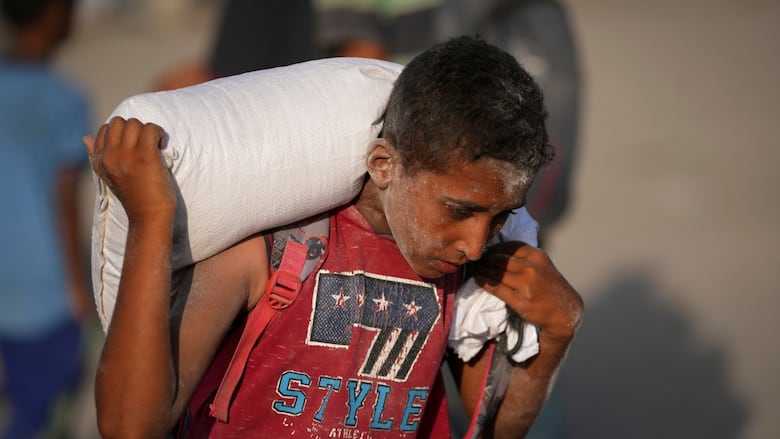 A Palestinian boy carries a sack of flour.
