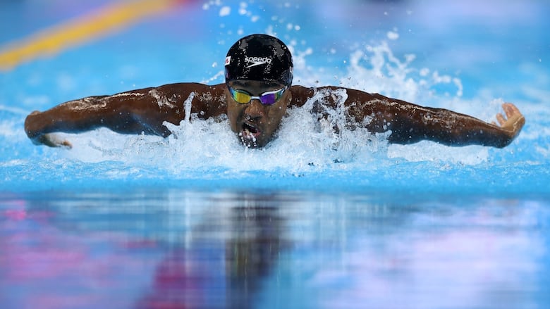 A male swimmer speeds through the water during a butterfly race as water splashes around him.