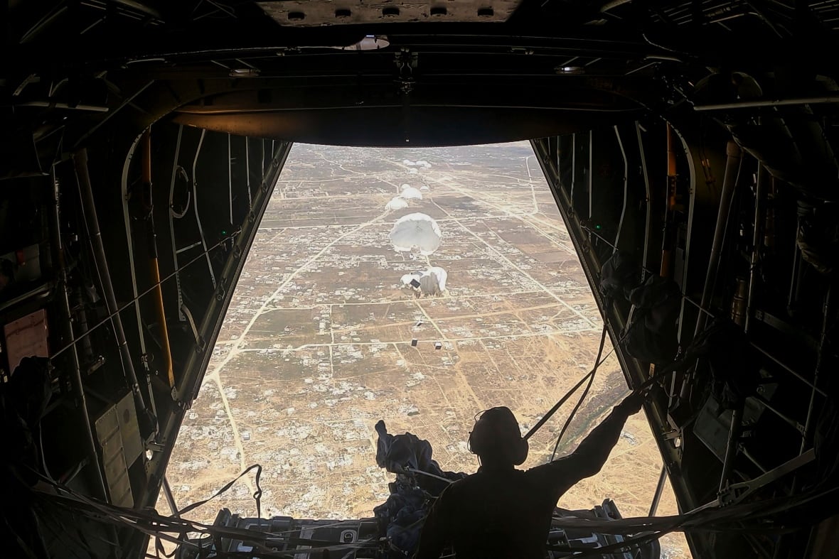 View of humanitarian aid being dropped over Gaza seen from inside the belly of an aircraft and a person standing by an opening.