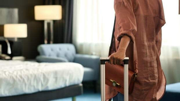 Close up of unrecognizable Black woman entering hotel room and holding suitcase upon travelling to resort.
