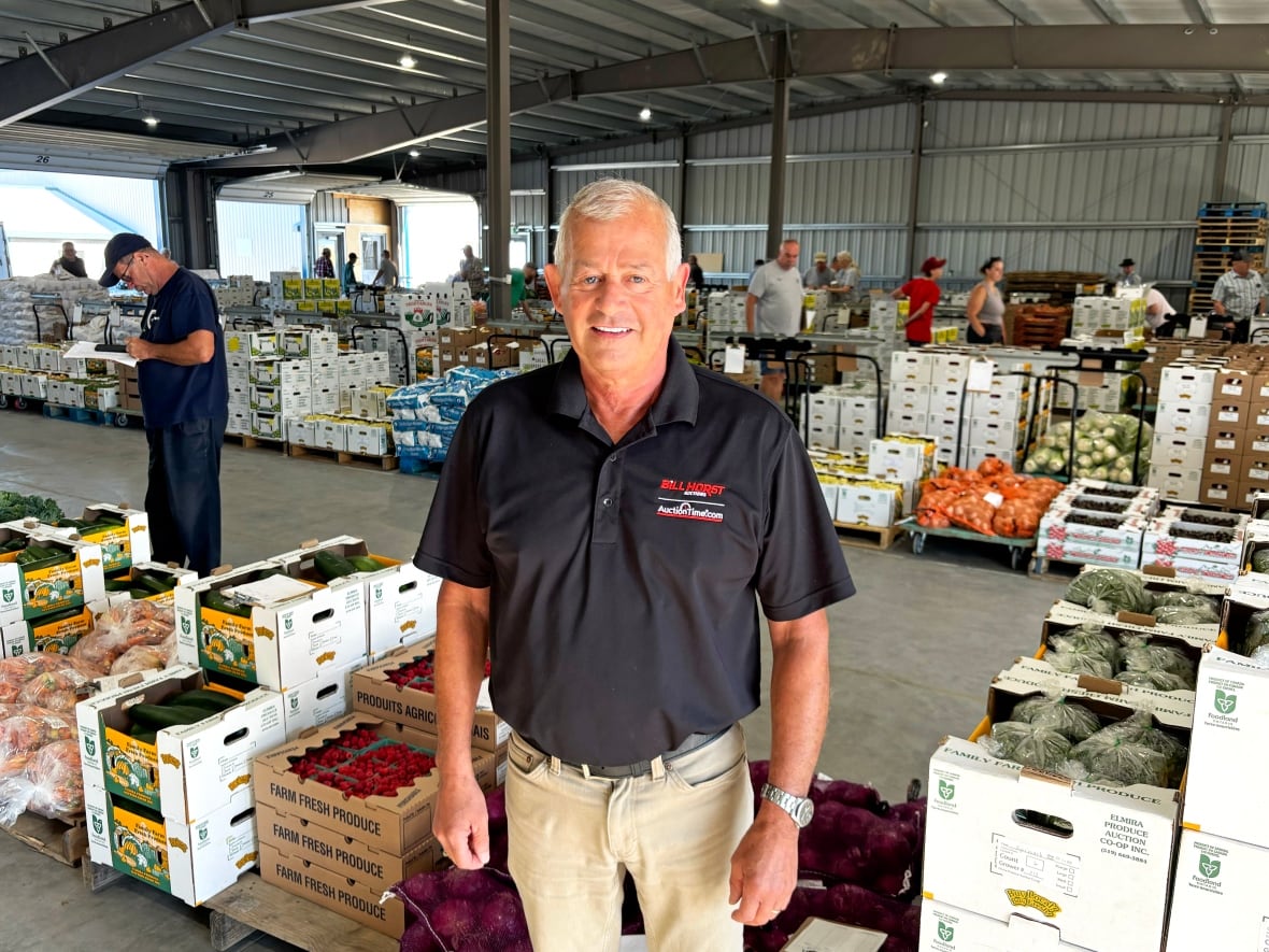 A man stands facing the camera while standing in the middle of a live produce auction.