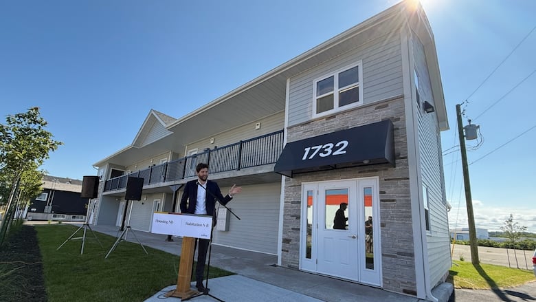 A man standing at a podium with a two-storey building in the background.