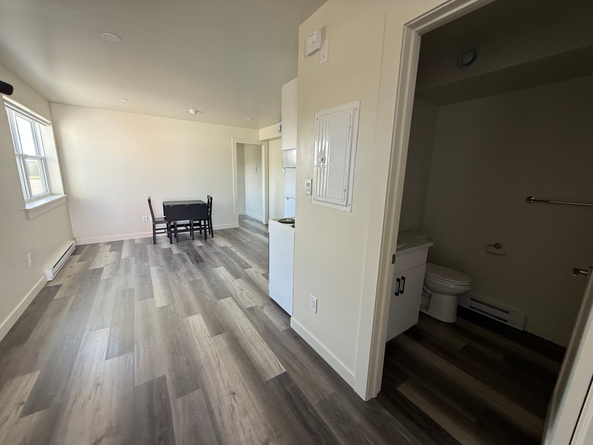 A largely empty room with a small kitchen, table and chairs, and a bathroom. 