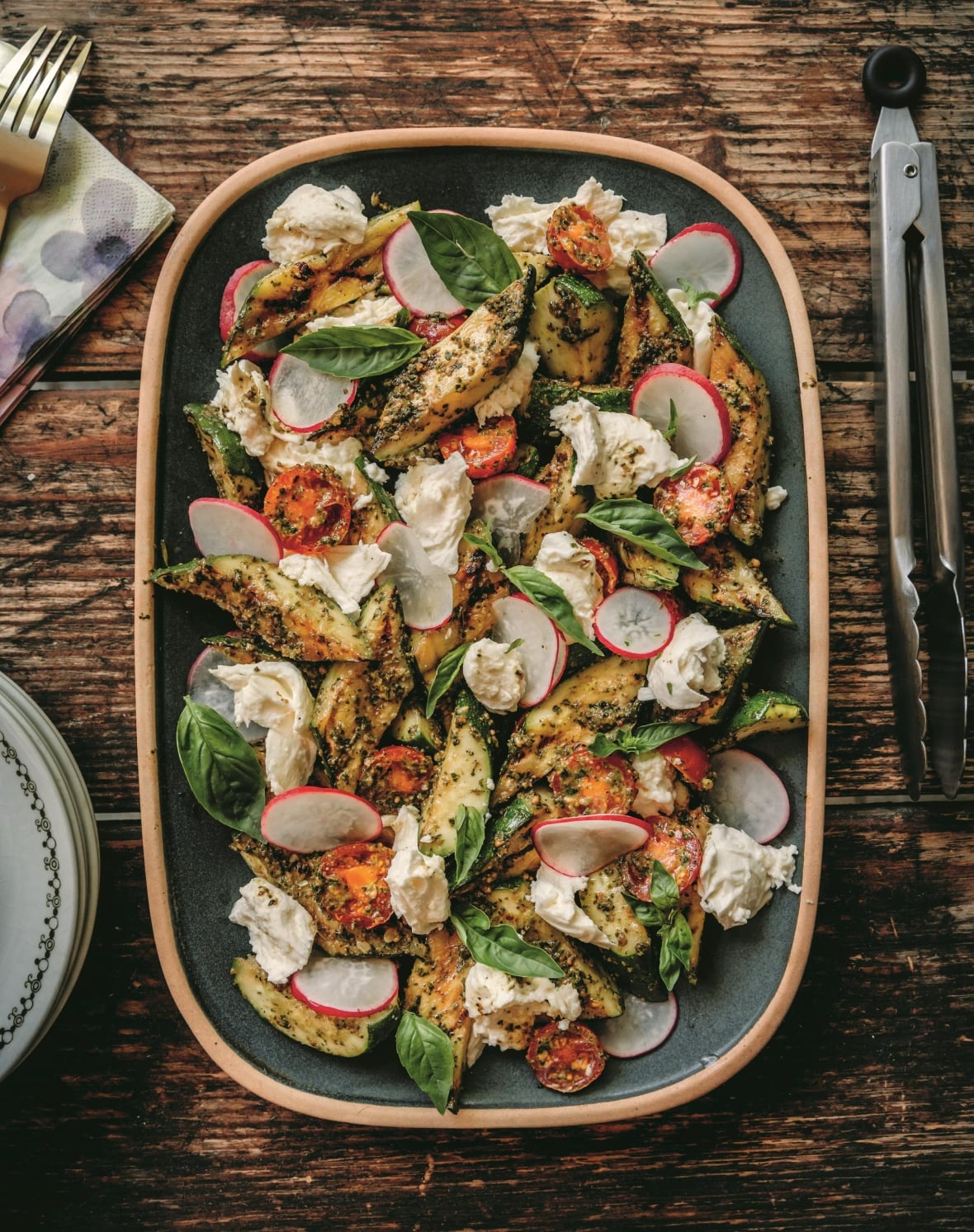 Top down shot of a platter of Grilled Zucchini & Mozzarella Salad with Pesto on a wooden table.