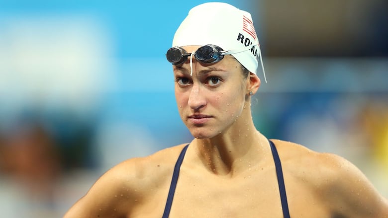 A female swimmer stands poolside with goggles above her eyes.