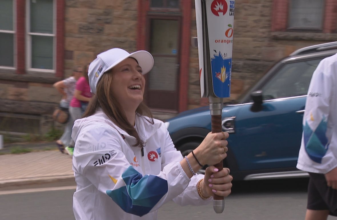 A smiling woman holding a large torch walks up a hill.