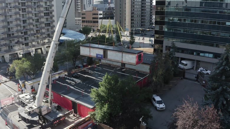 A rectangular modular housing unit is craned into place.