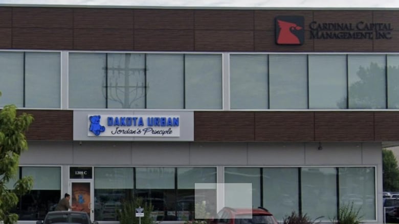 A photo of cars in a parking lot with a building that has the sign Dakota Urban Jordans Principle.