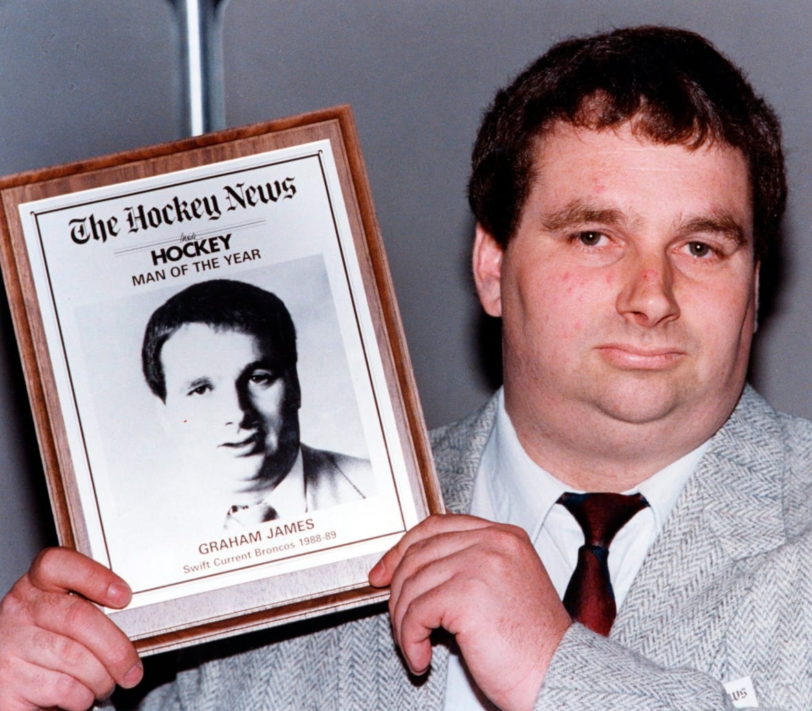 A man wearing a grey suit shows off a plaque with his face on it.