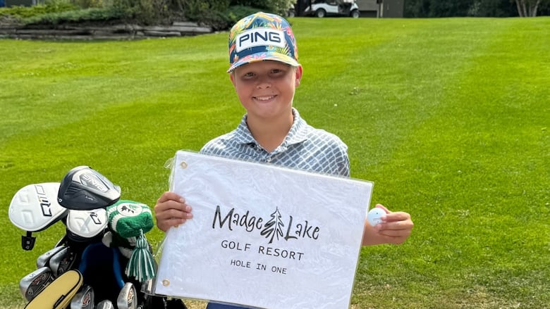 Krosby Jackman stands on a golf course holding up a flag and golf ball.