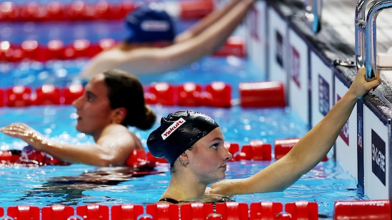A dejected female swimmer holds the ladder at the end of her lane after a race.