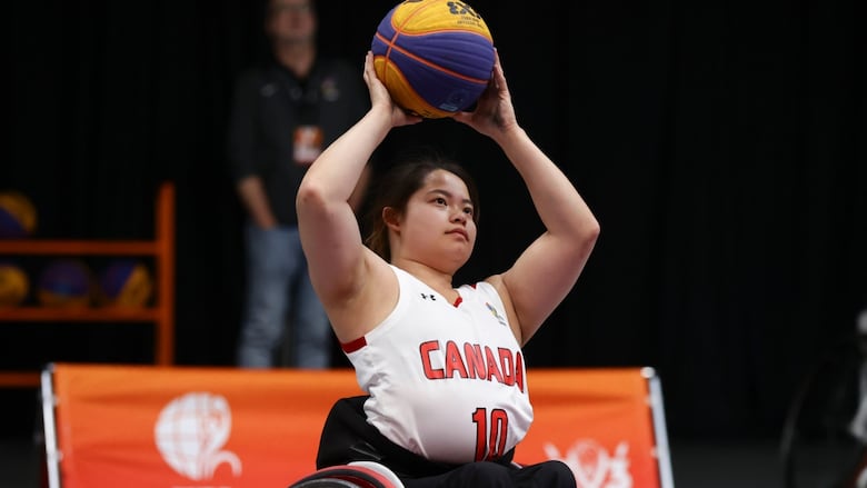 A female wheelchair basketball player wearing number ten representing Canada holds the ball above her head with both hands during a game.