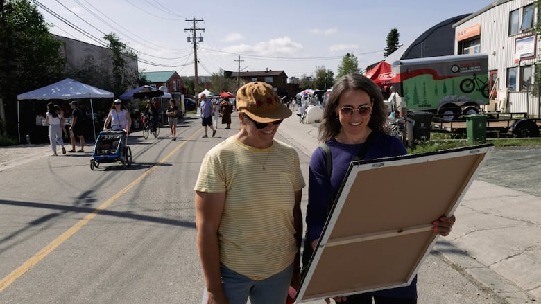 Two women look at a canvas print while standing in a busy street.