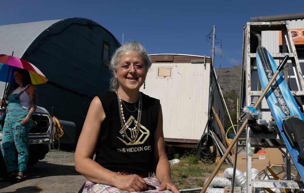 Woman sitting in the sun in a black tank top smiling at the camera.