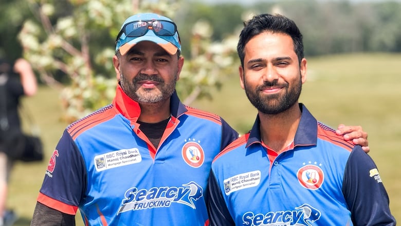 Two men wearing bright blue and red sports jerseys stand together on a green field.