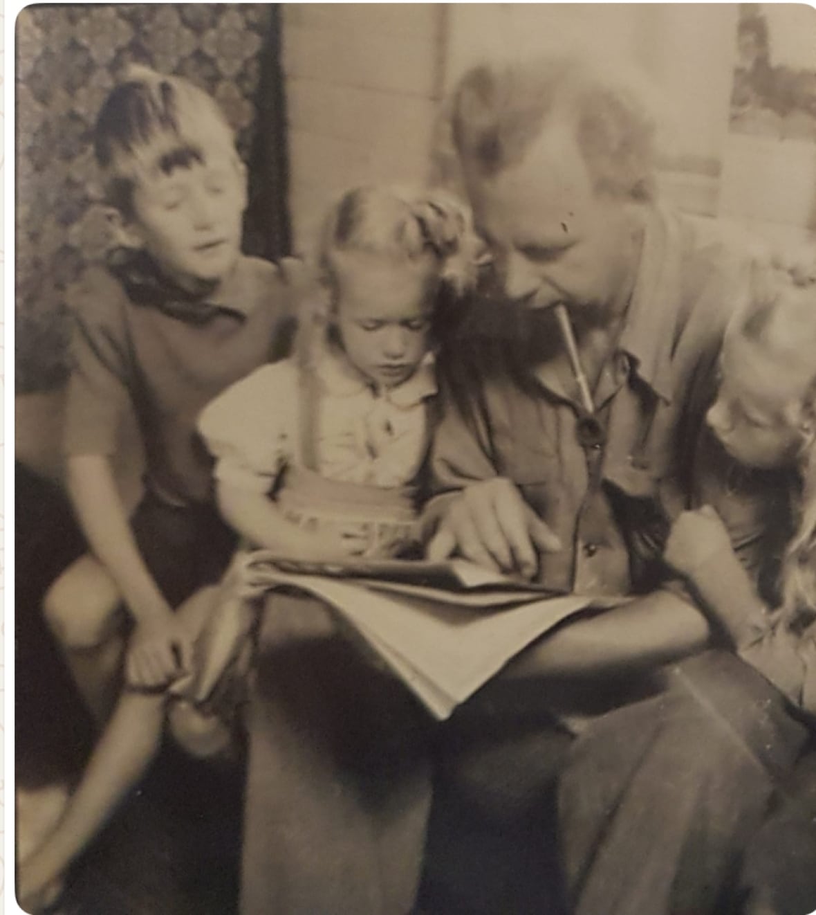 A black and white photo of a man who reads a book to three boys, a boy and two girls.