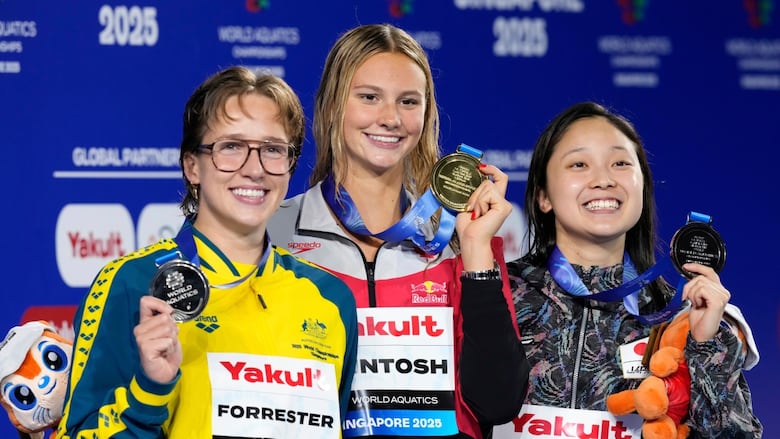 Three women stand on a podium displaying their medals.