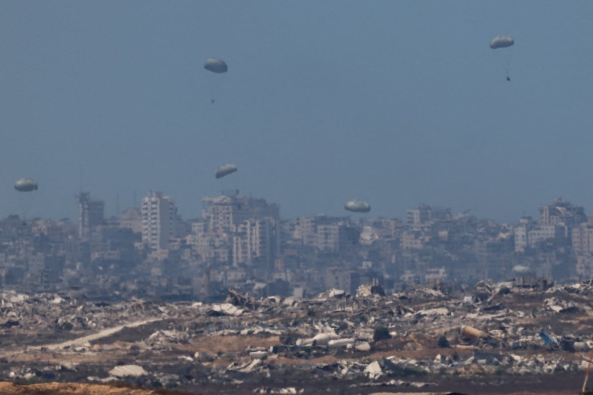Parachutes carrying aid fall over a destroyed city.