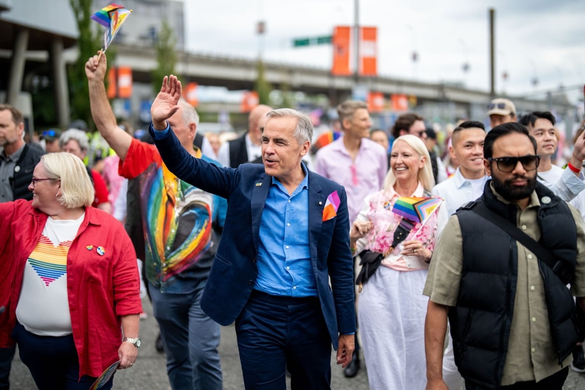 Prime Minister Mark Carney waves while he marches in the parade.